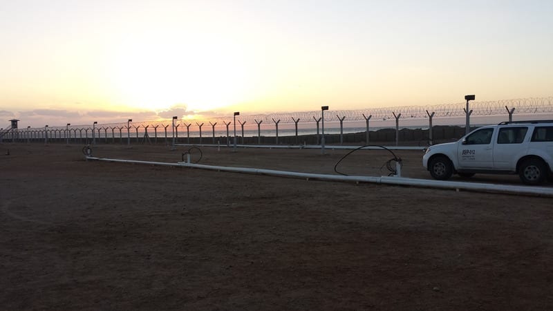 Remediation conveyance piping running across a fenced project site at sunset with a utility truck
