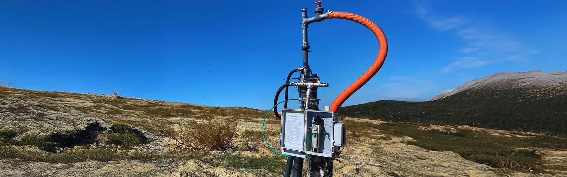 Landfill gas extraction wellhead with control box and flexible conveyance hose on a hillside